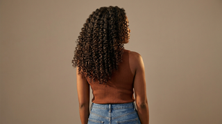Woman with healthy, defined natural curls shown from behind in a rust-brown top